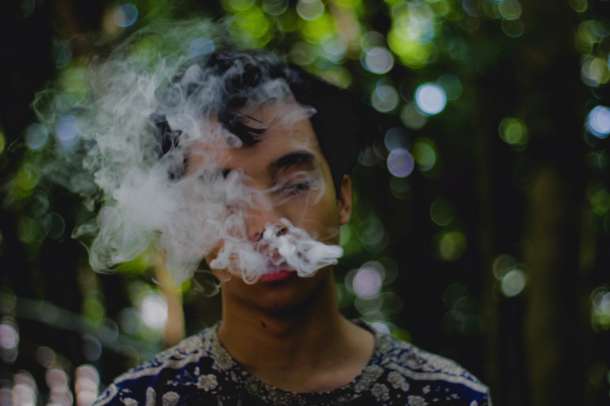 Hombre de cabello negro con humo en la cara saliendo de su boca