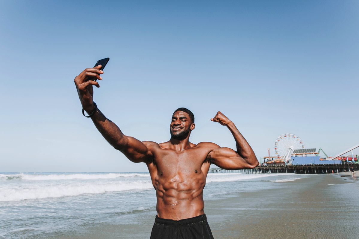 Hombre sin playera tomándose una selfie en la playa